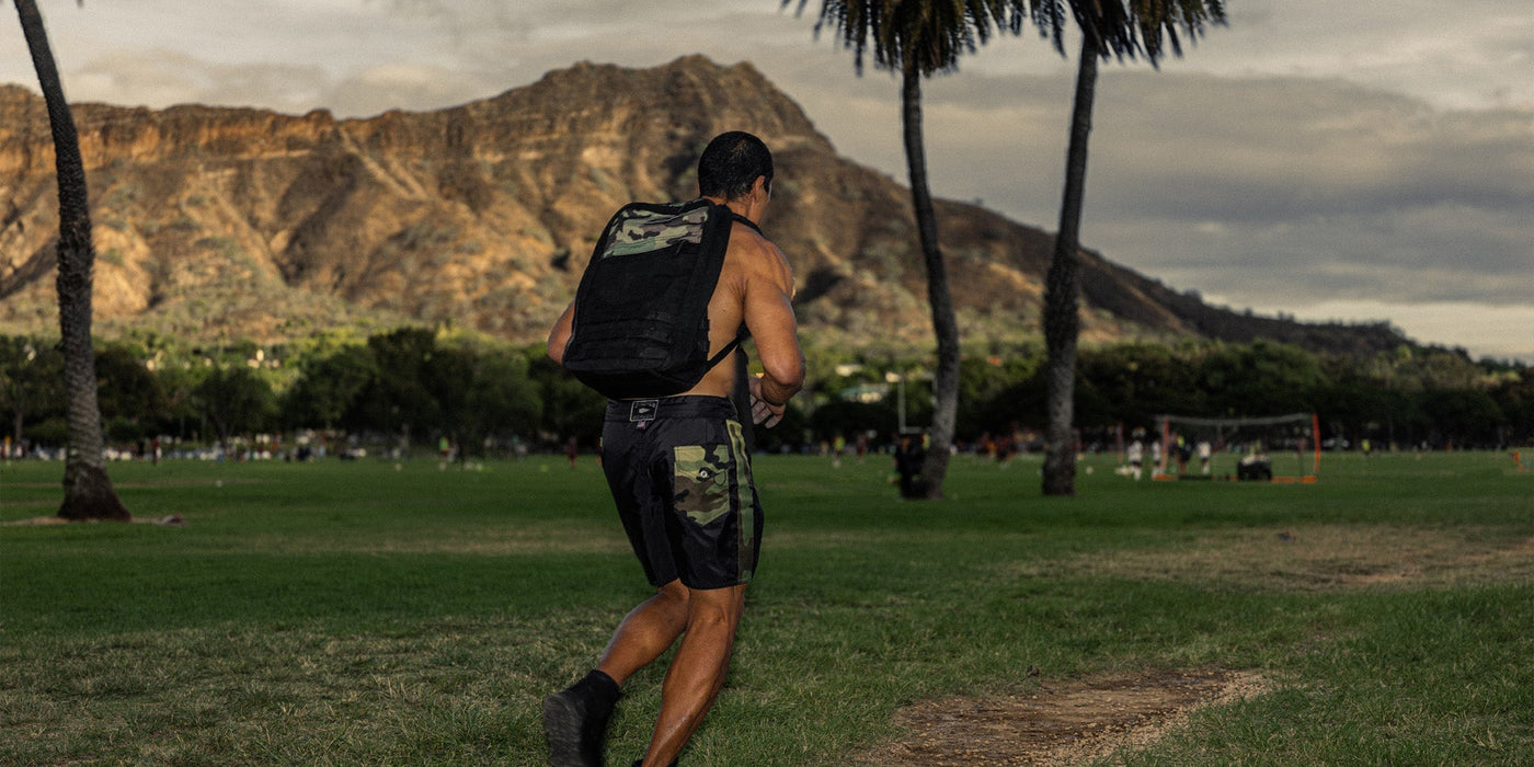 Man jogging with a backpack in a park, with a mountain in the background.