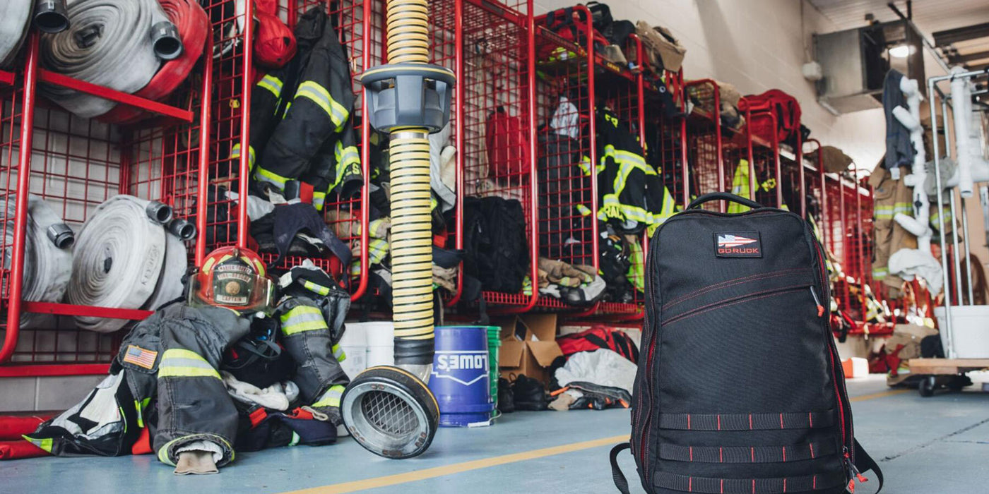 Firefighter gear and backpacks are stored in a fire station with red cages and hoses.