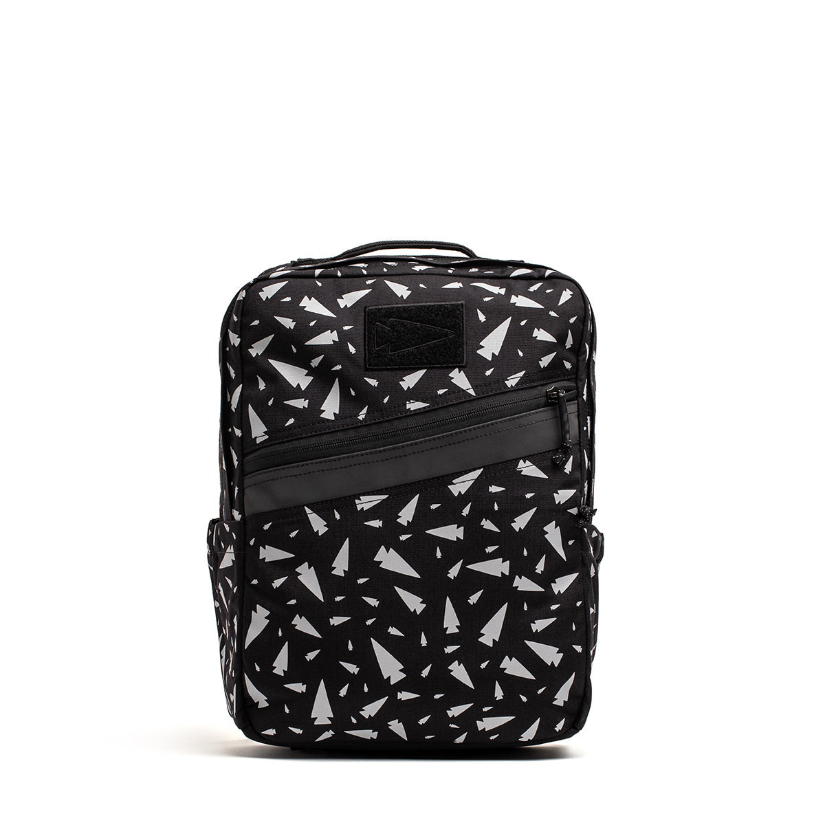 The KR1 - Spearhead Splatter by GORUCK is a kids' rucksack in black, adorned with a white paper airplane pattern. It features a front diagonal zipper pocket, a top handle for easy carrying, and textured fabric design that includes side pockets, perfect for school supplies.