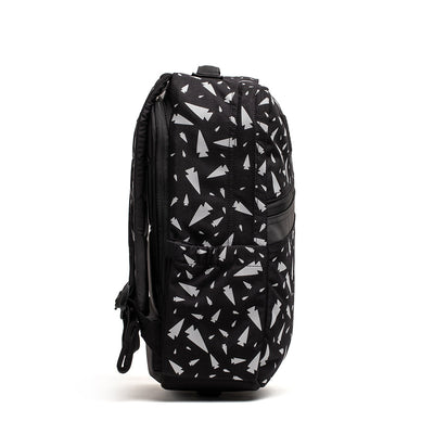 Side view of the KR1 - Spearhead Splatter, a black book bag by GORUCK with white geometric patterns, featuring multiple compartments, a padded back, and adjustable straps. This kids' rucksack is standing against a plain white background.