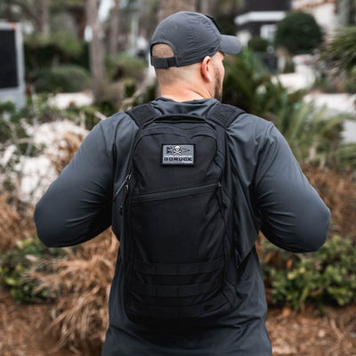 A person in a black jacket and cap stands outdoors, wearing the Bullet Ruck Classic - Cordura backpack, featuring a streamlined design that hints at being the perfect 15L daypack.