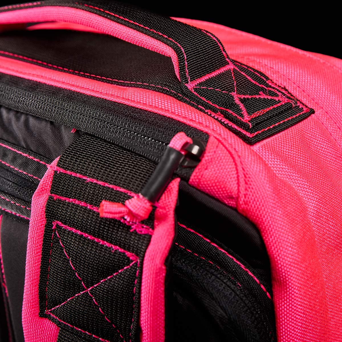 Close-up of the GORUCK GR1 USA backpack in vibrant hot pink and black, featuring reinforced stitching, adjustable straps, and a zipper. The detailed view highlights its toughness and style, focusing on the handle and zip area against a black background, showcasing its performance-ready design.