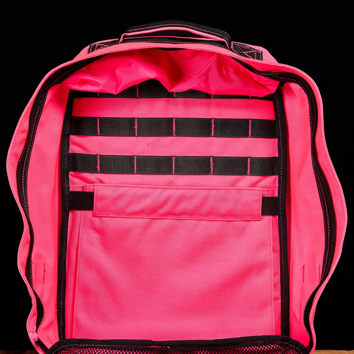 The GR1 USA - Hot Pink backpack from GORUCK, featuring multiple compartments and black straps, is showcased against a black background to highlight its performance and toughness.