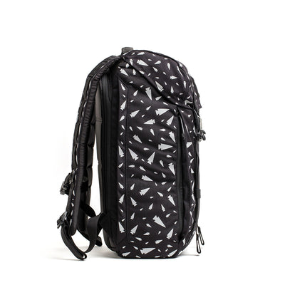 The GORUCK M23 - Cordura - Spearhead Shrapnel, a black rucksack with white geometric patterns seen from the side, is crafted from durable materials. It features padded shoulder straps and multiple zippers, evoking the rugged style of an M1945 Field Pack.