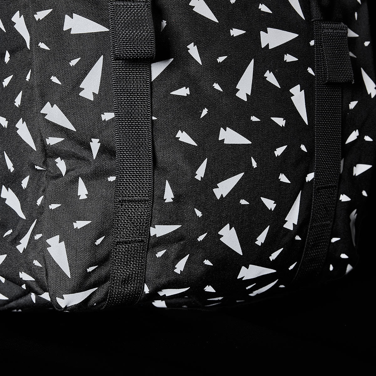 Close-up of the M23 - Cordura - Spearhead Shrapnel by GORUCK, showcasing a black fabric featuring a pattern of white abstract shapes resembling paper planes. This design is enhanced by intersecting black straps that add texture and highlight the use of durable materials in this geometric print.