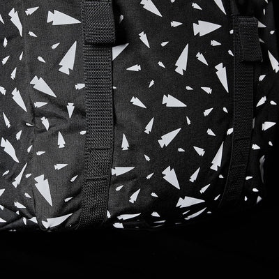 Close-up of the M23 - Cordura - Spearhead Shrapnel by GORUCK, showcasing a black fabric featuring a pattern of white abstract shapes resembling paper planes. This design is enhanced by intersecting black straps that add texture and highlight the use of durable materials in this geometric print.