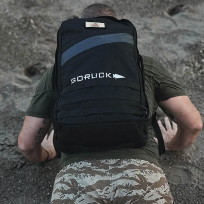 On the sand, someone is doing push-ups while wearing a Rucker 4.0 backpack from GORUCK, highlighting their dedication to rucking in difficult conditions.