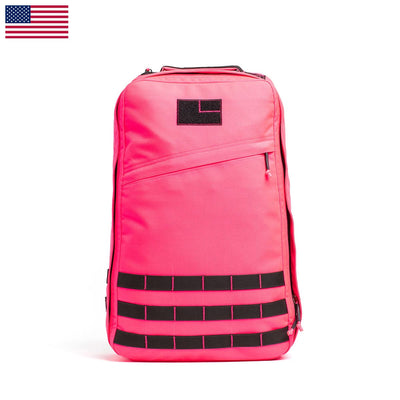 The GR1 USA - Hot Pink backpack by GORUCK features a bright pink design with a subtle black logo. It includes a diagonal front zipper pocket and black horizontal straps near the bottom. An American flag on the top left corner adds a hint of toughness, making it perfect for handling any adventure and meeting your daily demands.