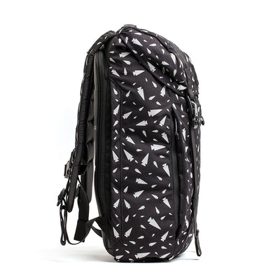 The side view of this black M23 - Cordura - Spearhead Shrapnel rucksack from GORUCK showcases white triangular patterns. Featuring adjustable straps, a side handle, and a zippered compartment, its modern design is ideal for students or travelers looking for both style and practicality.