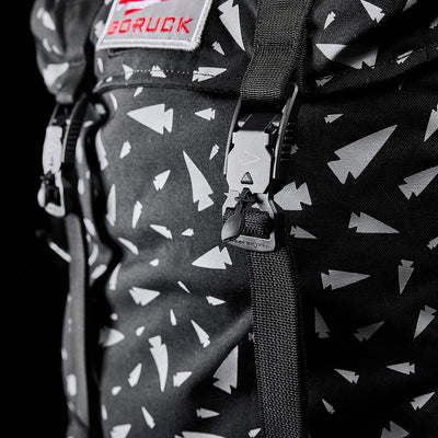 Zoomed-in view of the GORUCK M23 - Cordura - Spearhead Shrapnel, a contemporary rucksack adorned with white arrow patterns, constructed from durable materials, and equipped with straps and buckles.