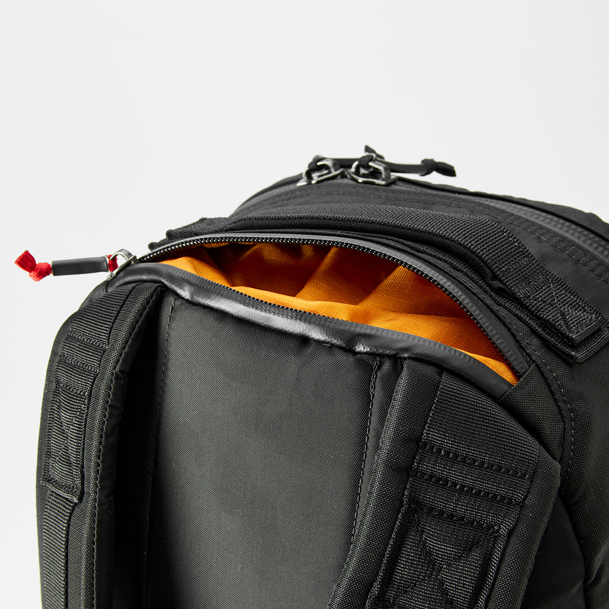 The Bullet Ruck - Ripstop ROBIC® - Michael Easter showcases a sleek black exterior with an open pocket, revealing a vibrant orange lining. Made from durable 420D ROBIC® Ripstop Nylon, it’s lightweight yet stylish and resilient against a plain backdrop.