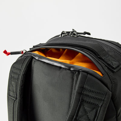 The Bullet Ruck - Ripstop ROBIC® - Michael Easter showcases a sleek black exterior with an open pocket, revealing a vibrant orange lining. Made from durable 420D ROBIC® Ripstop Nylon, it’s lightweight yet stylish and resilient against a plain backdrop.