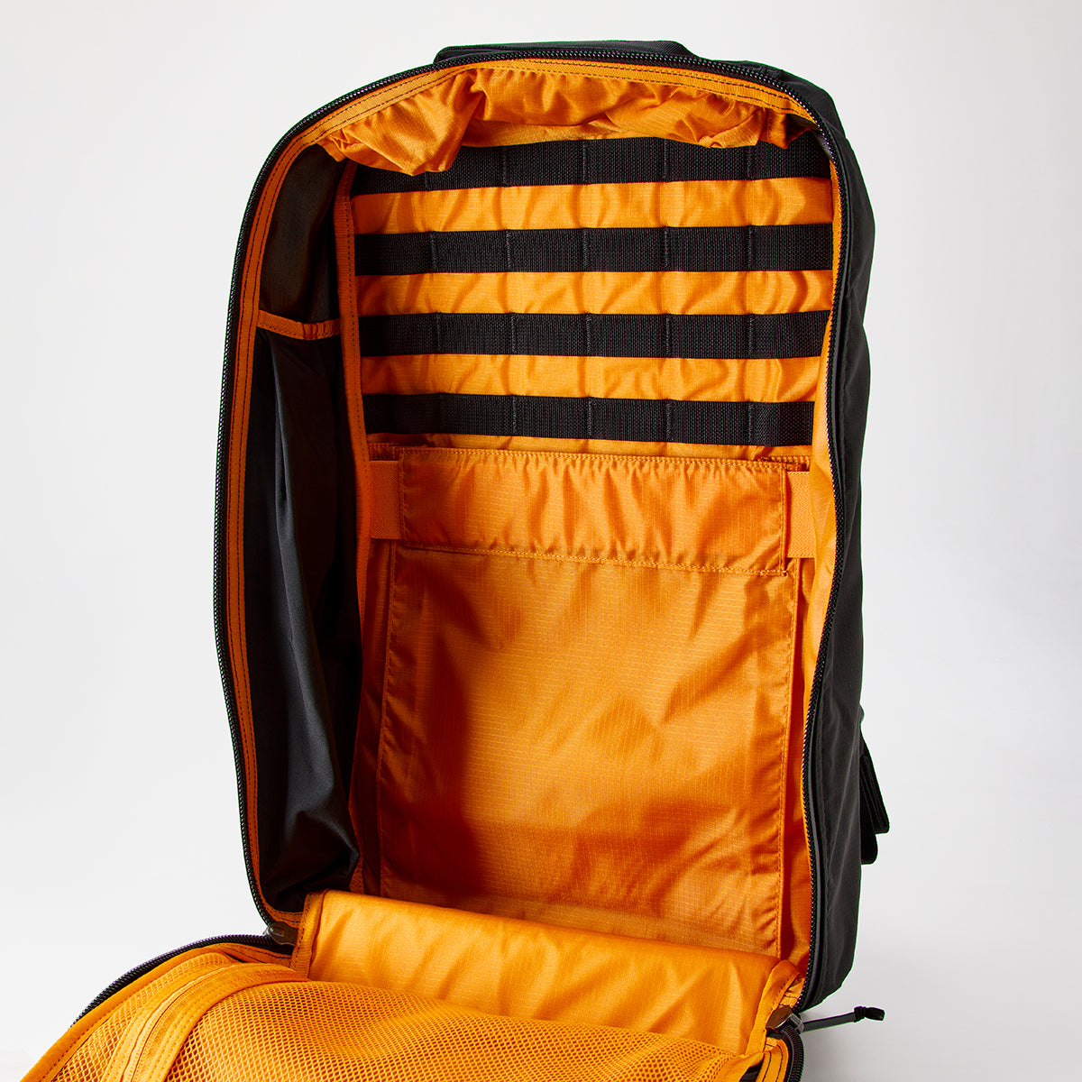 The GR2 - Ripstop ROBIC® - Michael Easter is a black travel ruck with an orange interior, made from tough 420D ROBIC Ripstop Nylon. It features multiple compartments on a light background and includes the Scars Lifetime Guarantee.