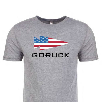 The "T-shirt - GORUCK USA - Grey" features a tri-blend material with an arrow design showcasing the U.S. flag and bold "GORUCK" text, honoring Special Forces.