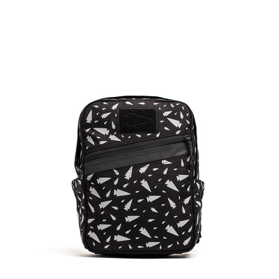 The KR1 - Spearhead Splatter by GORUCK is a black backpack ideal for school supplies, showcasing a scattered white geometric pattern and accentuated with a horizontal black leather strip across the front. It also includes side pockets and a small front pocket for added convenience.