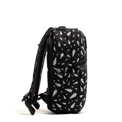 A side view of the KR1 - Spearhead Splatter kids' rucksack by GORUCK, showcasing a black design with white geometric patterns. It features adjustable straps and a zippered pocket on the side, all set against a white background.