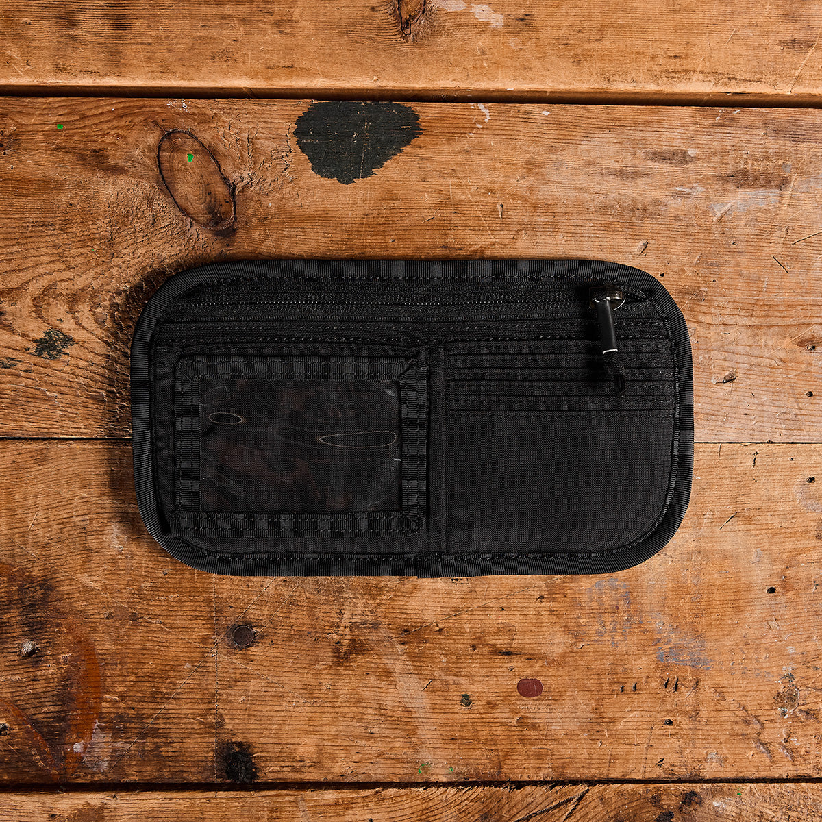 Introducing the GORUCK Admin Panels: a sleek black fabric wallet featuring a zippered compartment and multiple card slots, ideal for travel or EDC. It is showcased on a textured wooden surface.