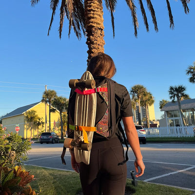 A person with a GR0 Skate Ruck - Built By SCARS from GORUCK, designed specifically for skaters, stands by a palm tree under a clear blue sky.