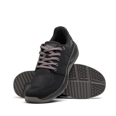 The Women's Ballistic Trainers from GORUCK, in Black + Black + Charcoal with Black Reflective Spearhead, highlight their robust CORDURA Ballistic Nylon and mesh design. One shoe is positioned upright while the other tilts to display its textured soles, underscoring the 3X Support feature for functional fitness enthusiasts.