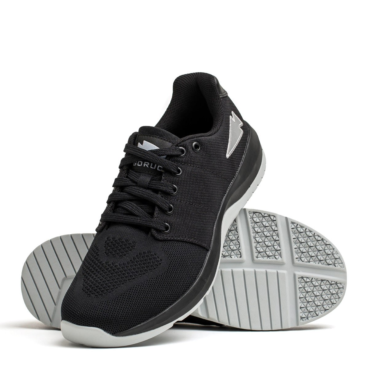 The GORUCK Men's Ballistic Trainers in Black with Glacier Grey and Silver Reflective Spearhead feature a robust design crafted from durable CORDURA® Ballistic Nylon. One shoe is positioned upright, revealing both the side and top views, while the other rests on its side to showcase the textured sole. This functional fitness footwear includes laces and displays the brand logo on the side.