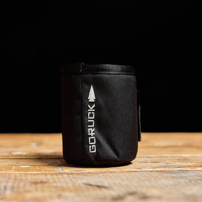 A GORUCK Ballistic Beer Jacket, made from 1000D CORDURA, sits on a wooden surface, its black color contrasting sharply with the background.