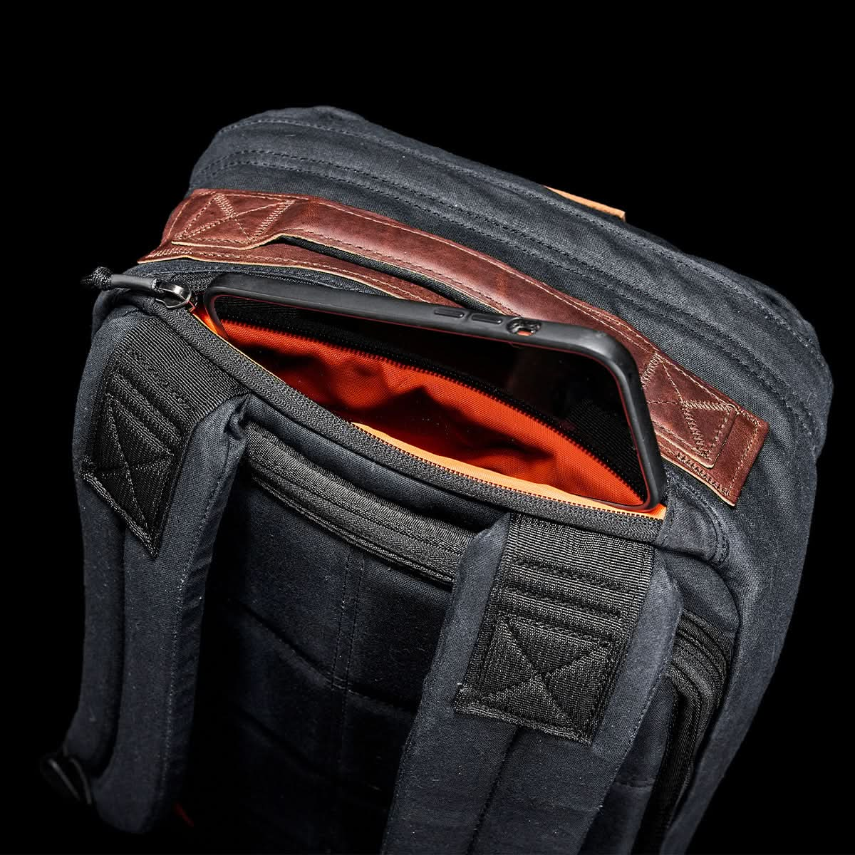 The GORUCK GR1 USA - Heritage rucksack, made from waxed duck canvas, features an exposed zipper that reveals an orange interior with a tablet partially inside.