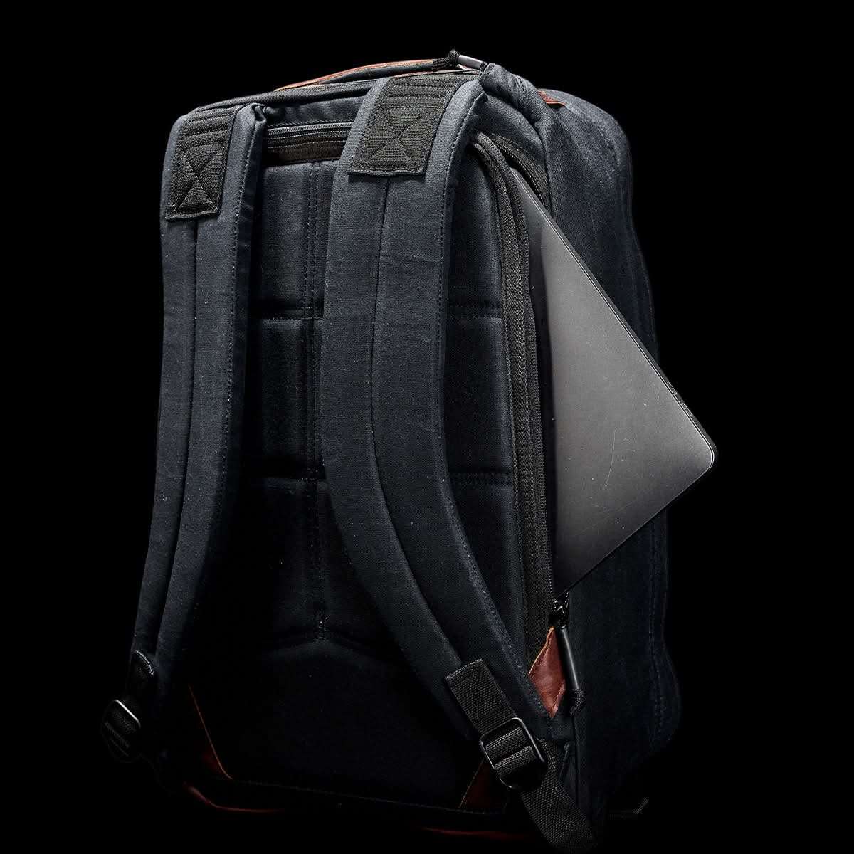 A GR1 USA - Heritage Rucksack by GORUCK, featuring two padded straps, displays a partially visible laptop in a side pocket set against a dark background.