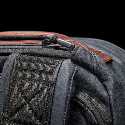 Close-up of the GR1 USA - Heritage rucksack by GORUCK, showcasing its black and brown zipper and strap made from durable waxed duck canvas, set against a dark background.