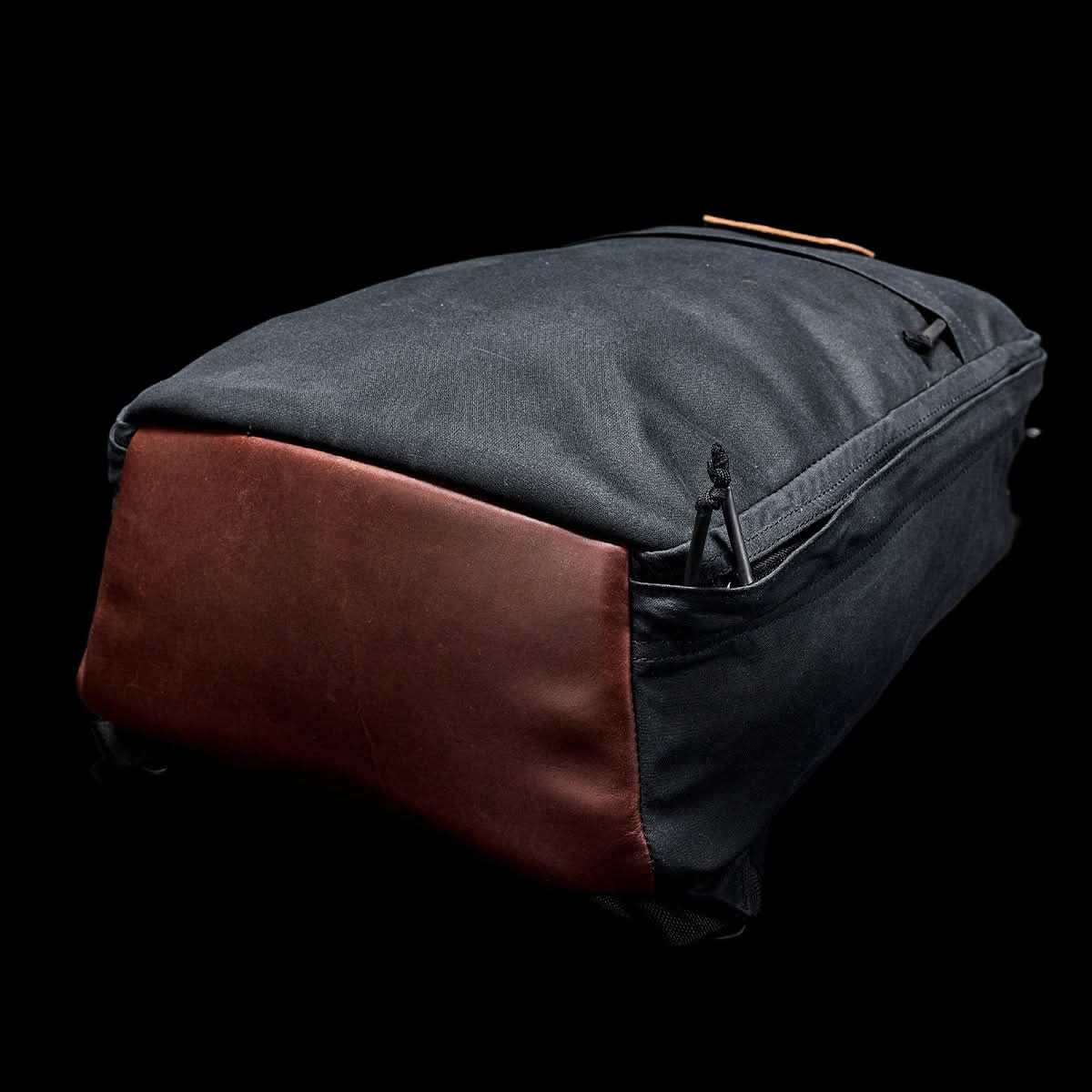 The GR1 USA - Heritage by GORUCK features a sleek black design with a brown leather bottom, beautifully displayed against a black backdrop.