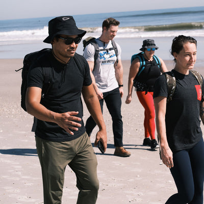 Four people stroll on a beach, smiling in their Slick Boonie Hats made with ToughDry® fabric, enjoying the sunshine and protection from the elements.