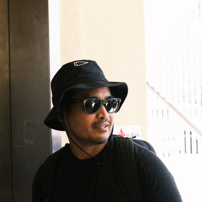 A person wearing sunglasses and a black Boonie Hat - Slick - ToughDry stands by an elevator, looking to the side. The hat offers superior protection from the elements, combining style and comfort for their urban adventure.