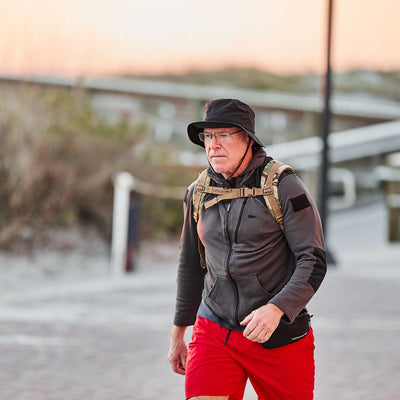 A person in red shorts and a Boonie Hat - Slick - ToughDry blends into the path background while walking outdoors with a backpack.