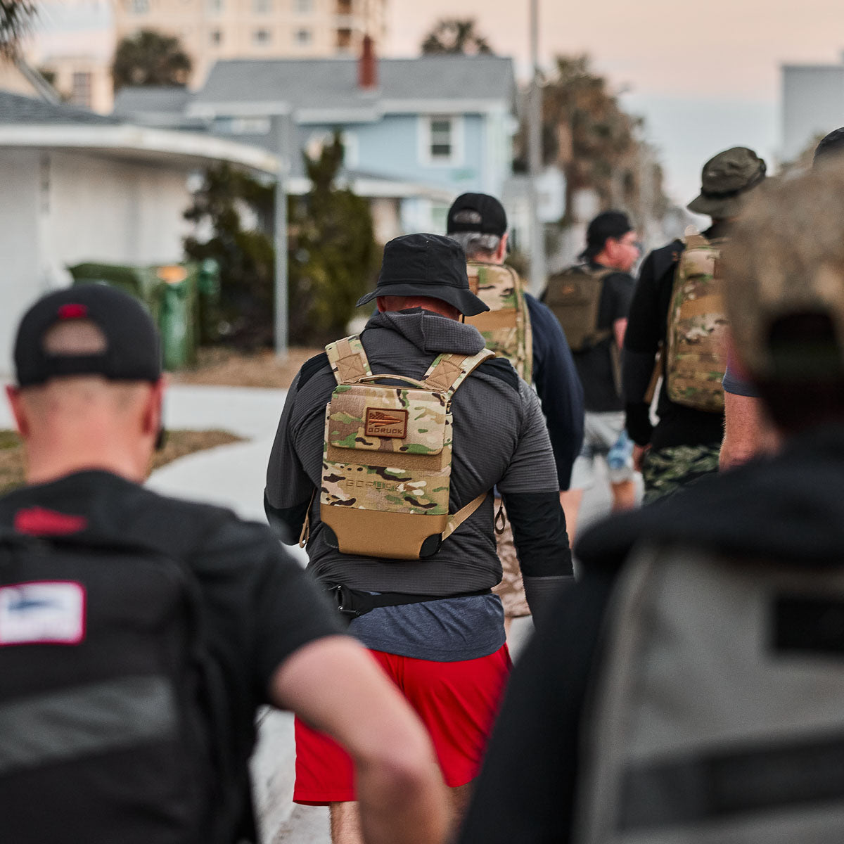 A group of people wearing Boonie Hat - Slick - ToughDry hats and backpacks strides down the sidewalk in an urban area, enjoying protection from the elements with their gear.