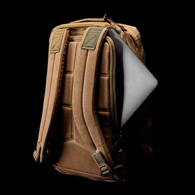 The GR1 USA - Heritage by GORUCK is a rucksack made from waxed duck canvas, showcasing a brown color with a visible laptop storage slot on a sleek black backdrop.