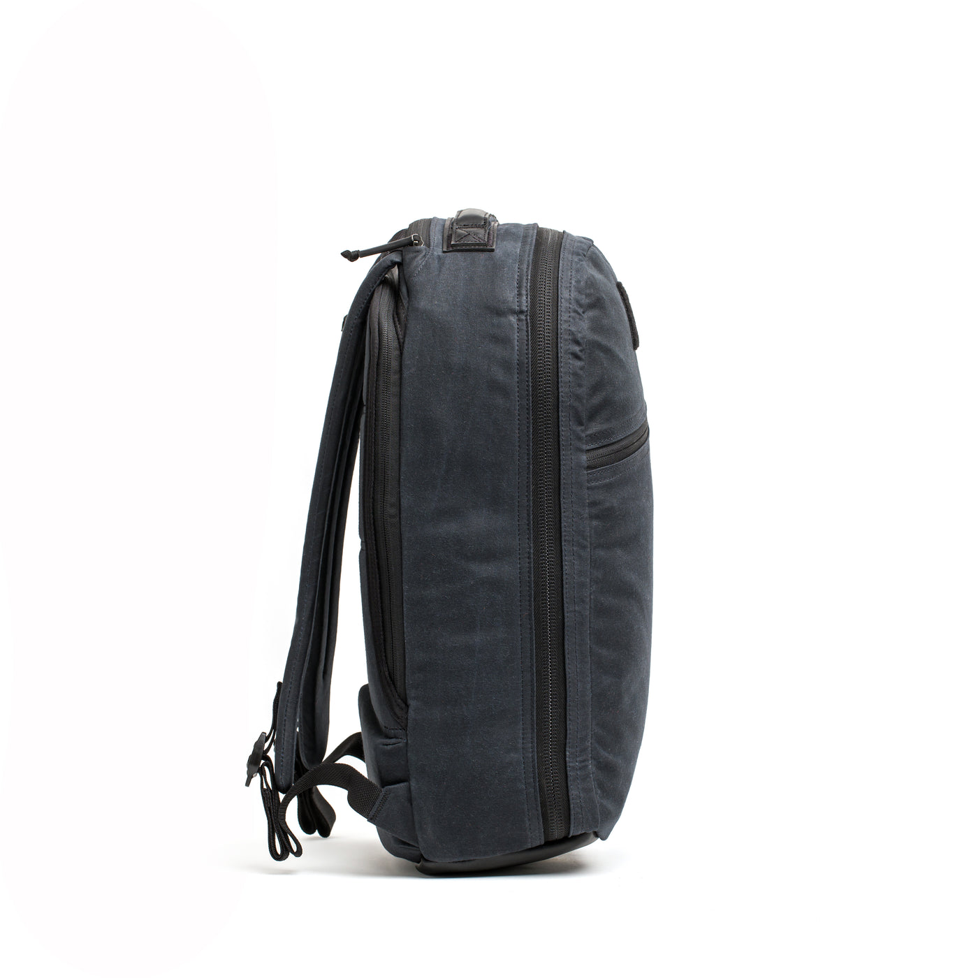 A side view of the Bullet Ruck - Waxed Canvas by GORUCK features a minimalist dark gray design with multiple zippers and adjustable shoulder straps, set against a plain white background. Its sleek and modern appeal is reminiscent of the classic retro canvas rucksack.