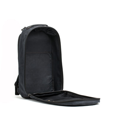 A GORUCK Bullet Ruck - Waxed Canvas backpack in black is displayed against a white backdrop. It showcases a main compartment with a zippered mesh pocket and multiple organizers, emphasizing its roomy interior and practicality for storage, reminiscent of a classic canvas rucksack design.