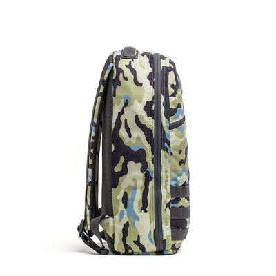 The side profile of the Bullet Ruck Classic - Cordura by GORUCK showcases a sleek daypack in a camouflage pattern with green, black, and blue hues, featuring a zipper. Its streamlined design is enhanced by padded straps for added comfort.