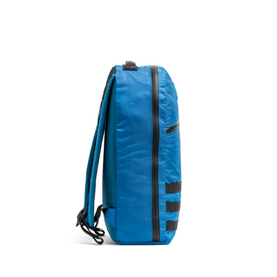 Side view of the Bullet Ruck - Ripstop ROBIC®, a blue 15L daypack with black zippers and extra padded straps, set against a white background.