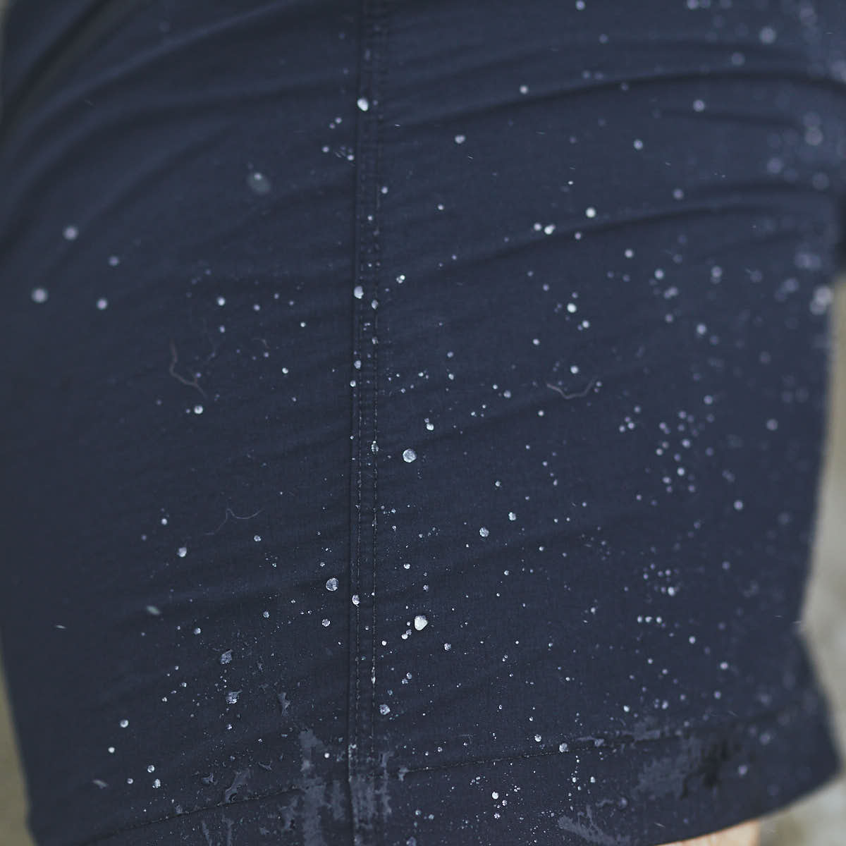 Close-up of a dark blue pair of Men’s Challenge Shorts - Lightweight ToughDry® from GORUCK, showcasing small water droplets on the surface, indicating that the material has been exposed to rain or splashes. The droplets form a pattern on the slightly crinkled fabric, highlighting its water-resistant qualities.