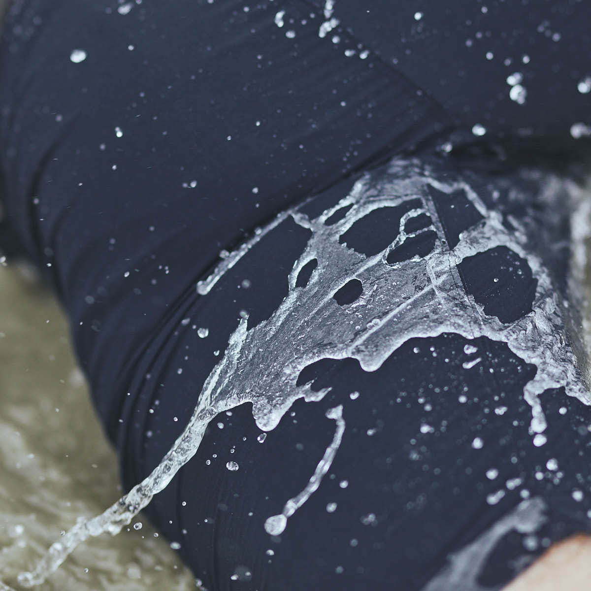 Water splashes onto a person wearing the GORUCK Men’s Challenge Shorts - Lightweight ToughDry® in dark fabric, perfectly capturing droplets in motion against the material. These shorts' cargo pockets provide a rugged appeal, while the diamond gusset ensures enhanced durability, with a blurred section of water visible in the background.