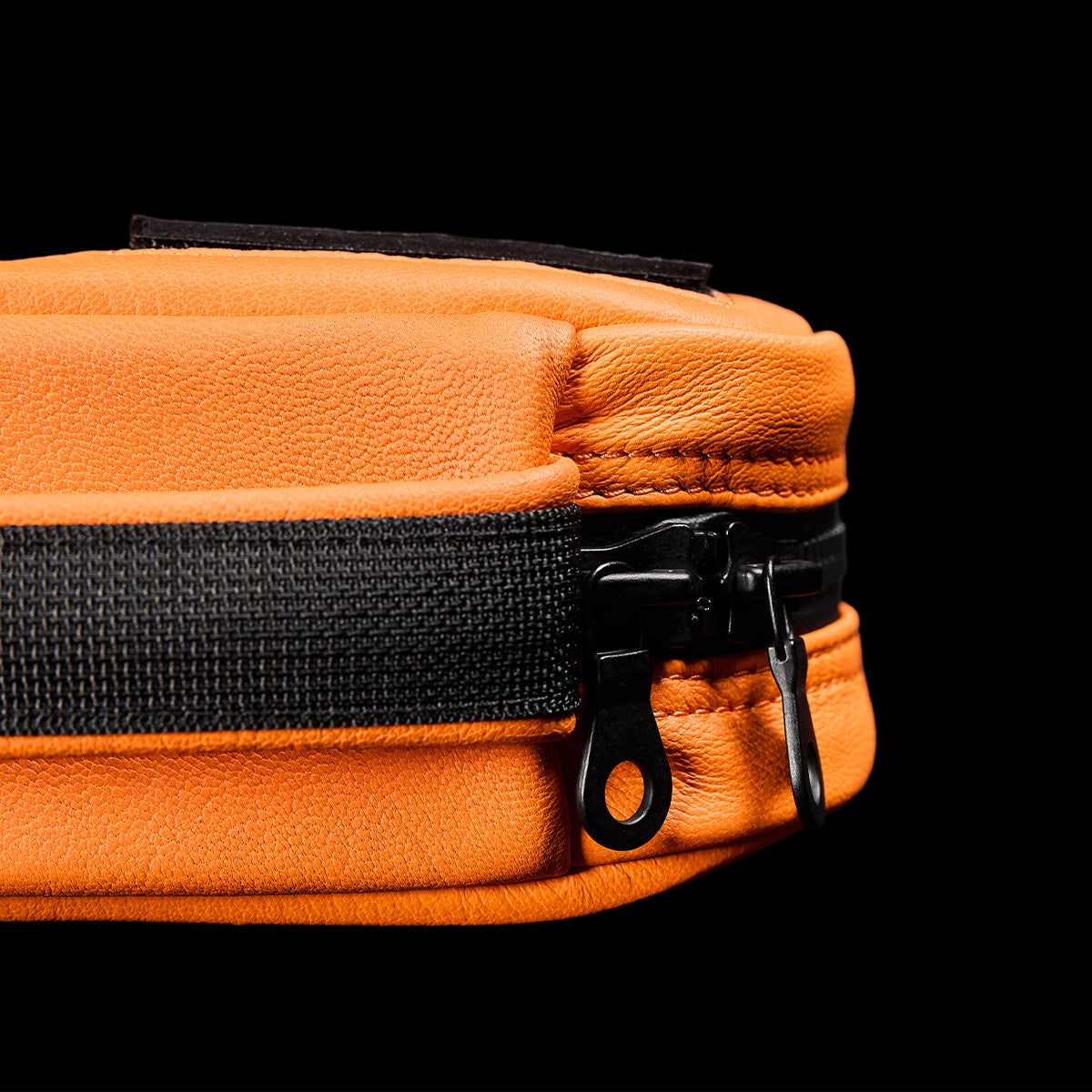 Close-up of the Echo Field Pocket x Carryology - Berserker Viking by GORUCK in orange leather, featuring a black zipper and strap against a black background. The texture of the leather and metallic zipper pulls echo the legendary craftsmanship of the Norsemen.