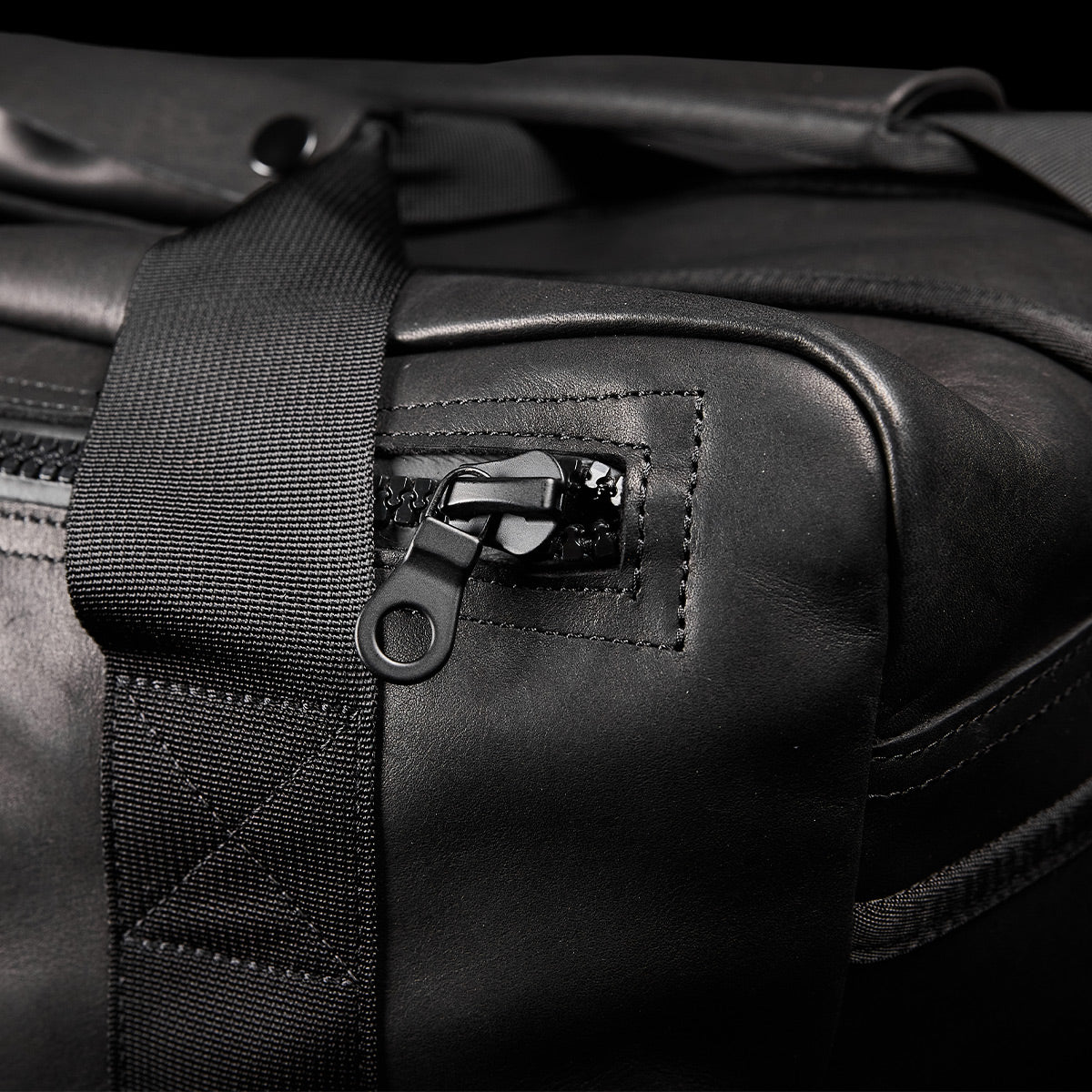 Close-up of the GORUCK Kit Bag x Carryology - Berserker Viking, featuring a textured black leather finish reminiscent of Viking armor. Highlighting the zipper pull, it is uniquely attached to a fabric strap that is expertly stitched onto the bag, showcasing craftsmanship and design elements akin to those prized by Norsemen warriors.