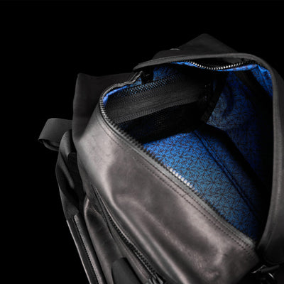 The Kit Bag x Carryology - Berserker Viking by GORUCK is an open black leather bag with a vibrant blue fabric interior, echoing the style of Viking armor and adorned with a geometric pattern. It includes a visible interior zippered pocket and robust black straps. Set against a solid black background, the striking details of this Viking-inspired accessory are prominently highlighted.