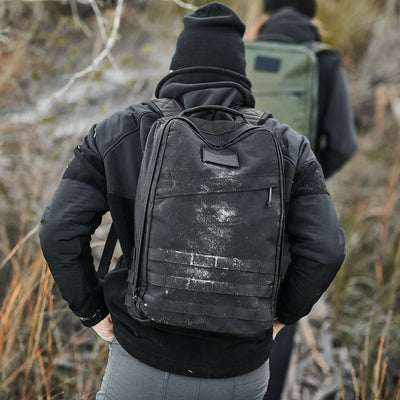 A person in a black hoodie and beanie, wearing the Men’s Task Force Dagger Jacket with Polartec fleece for warmth, hikes through tall grass and trees, their black backpack suggesting the readiness of Special Forces.