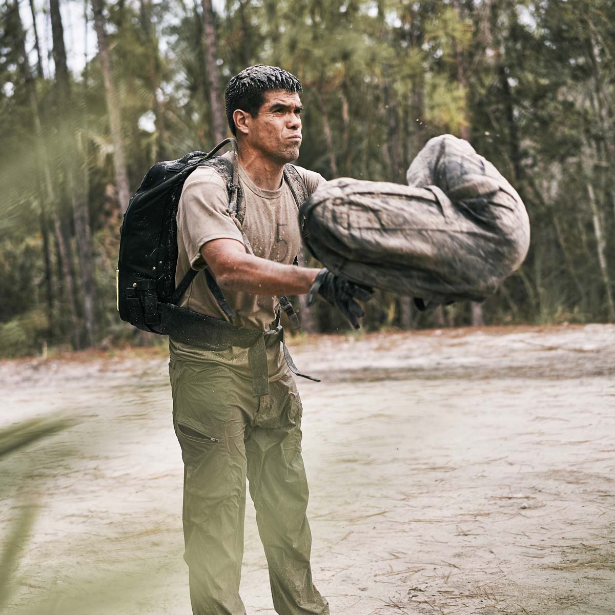 Wearing Men’s Challenge Pants in Lightweight ToughDry®, a man with abrasion-resistant fabric and ample cargo pockets carries a large sack through the wooded area.