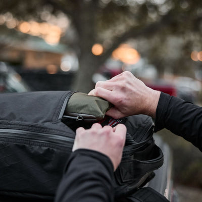 Gentle hands easily pack a green Packable Bullet Ruck - Ripstop ROBIC® into a black backpack outdoors.