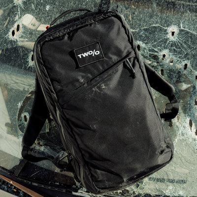 The GR2 - Ripstop ROBIC® - Michael Easter is a black backpack featuring the "TWO/O" logo on a shattered glass surface. Made from durable 420D ROBIC Ripstop Nylon, it promises rugged reliability with the Scars Lifetime Guarantee, ideal for both adventure enthusiasts and city explorers.