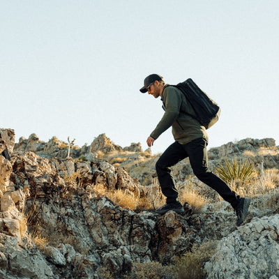 A man hikes over rugged terrain with a GR2 - Ripstop ROBIC® - Michael Easter, trusting its durable 420D ROBIC Ripstop Nylon and Scars Lifetime Guarantee for peace of mind.