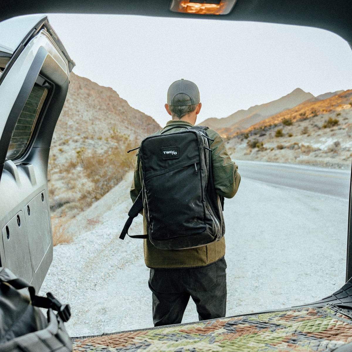 A person with the GR2 - Ripstop ROBIC® - Michael Easter backpack, made of durable 420D ROBIC Ripstop Nylon, stands by a desert road as seen from inside a vehicle.