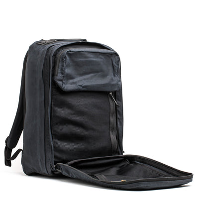 An elegant, dark gray GR2 - Waxed Canvas by GORUCK is displayed open, revealing its roomy interior with several compartments. Made from waxed duck canvas, it includes a front pocket and adjustable shoulder straps crafted from Red Wing leather, making it ideal for travel or everyday use.